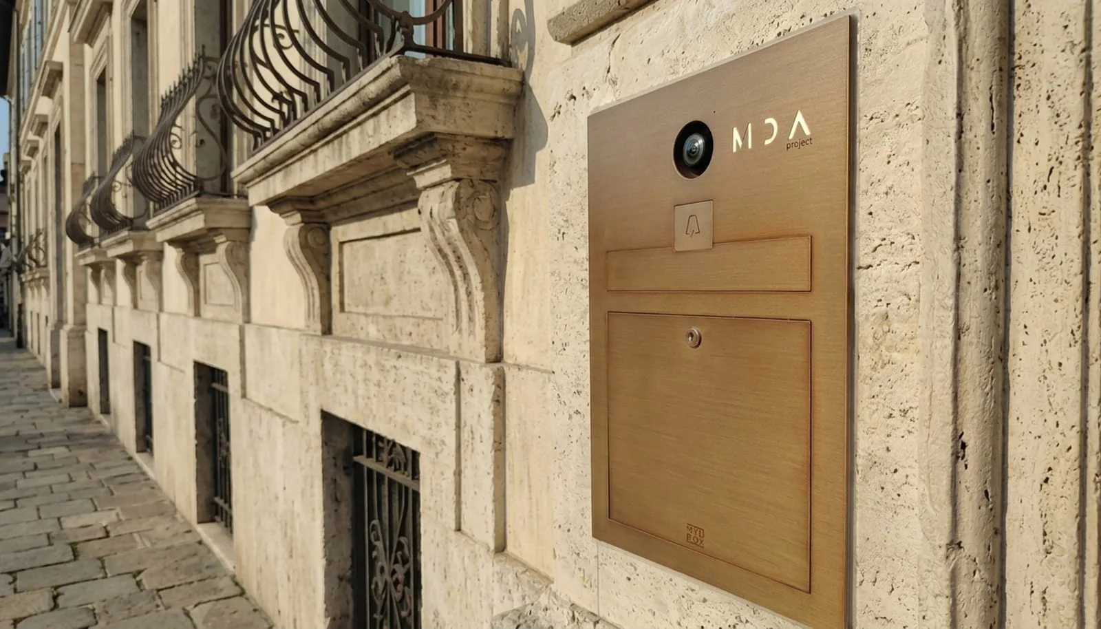 Made in Italy design mailbox, "Loos" model, with a bronze finish and video intercom, installed on the entrance wall of a historic building.